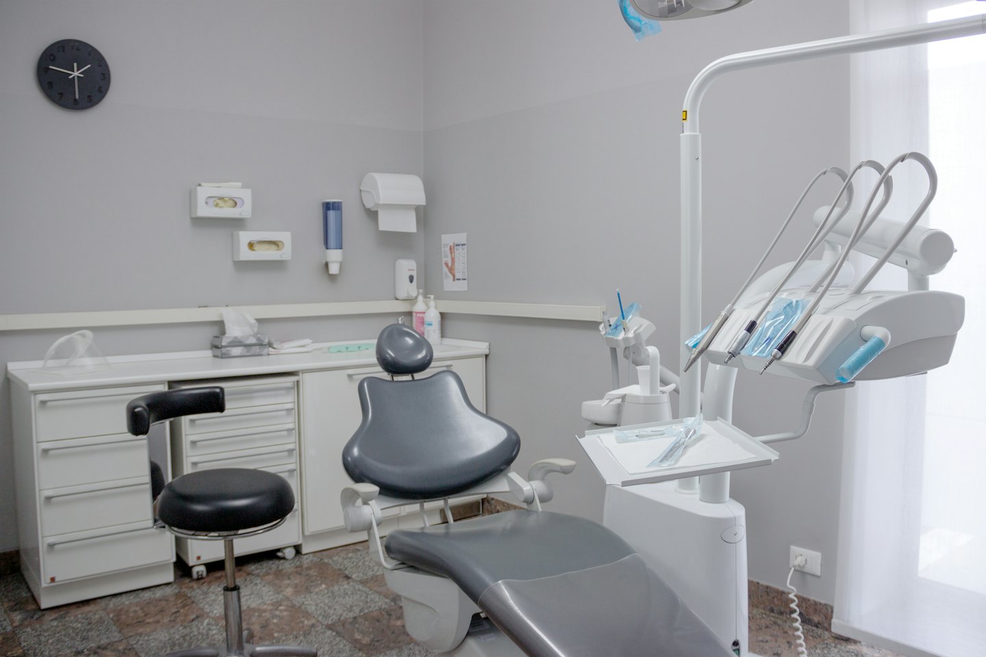 Modern empty dental exam room with grey chair and white equipment.